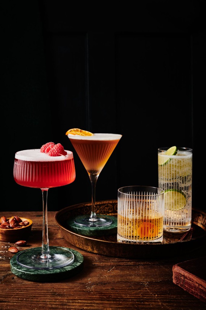 Four crafted mocktails in ribbed glassware on a dark wooden table